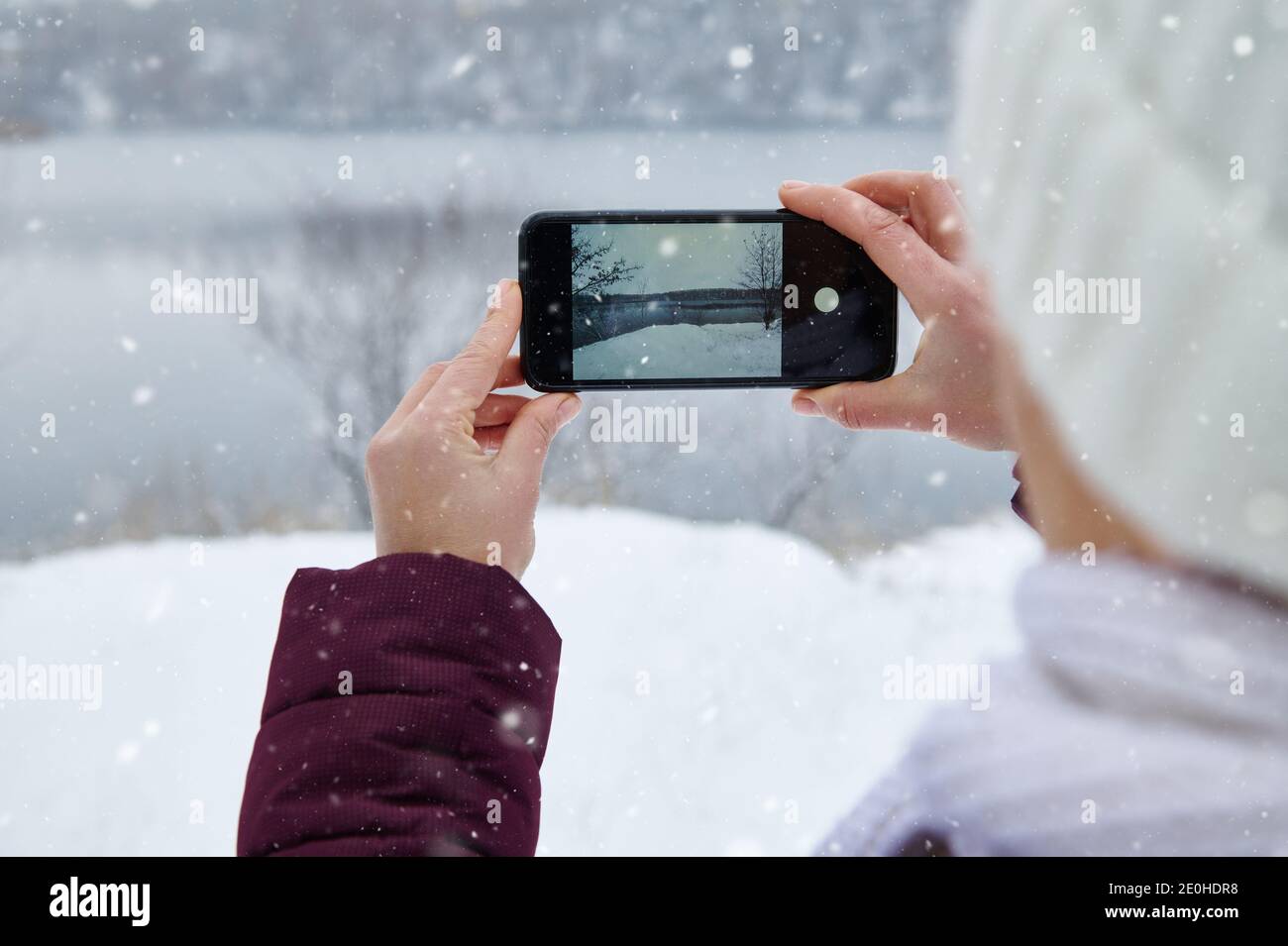 Nahaufnahme der Hände halten Smartphone und machen ein Shooting Der Natur beim Schneefall auf dem Hintergrund des Schnees Überdachte Landschaft Stockfoto