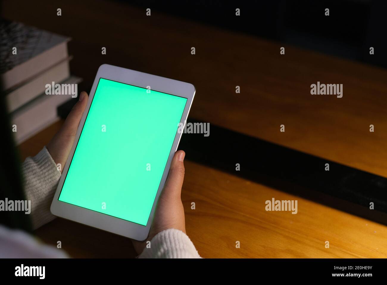 Über der Schulter Ansicht der Frau halten grünen Bildschirm Tablette neben Buchen Sie bei Nacht Stockfoto