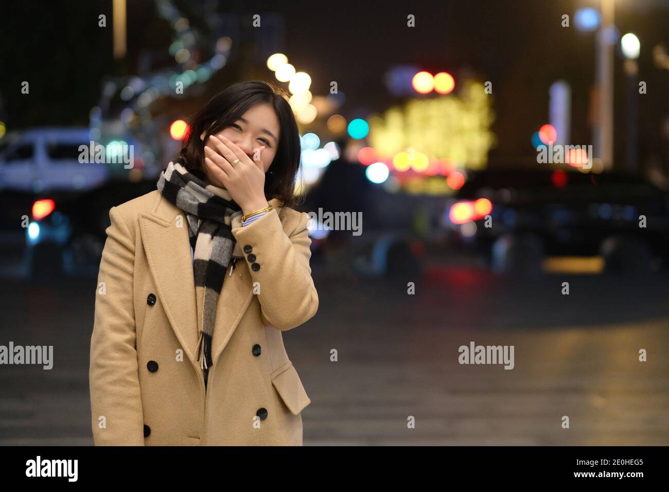Mittlere Aufnahme einer schönen asiatischen jungen Frau, die nachts hinter der Hand lacht. Stockfoto