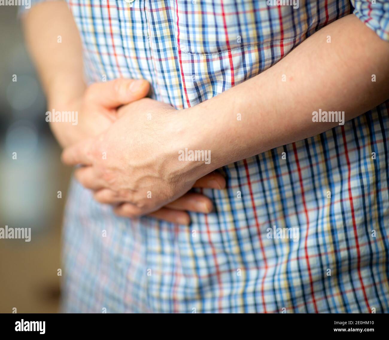 Mann mit Bauchschmerzen. Mann in einem Hemd, die Hände auf dem Bauch haltend, Nahaufnahme auf den Händen Stockfoto