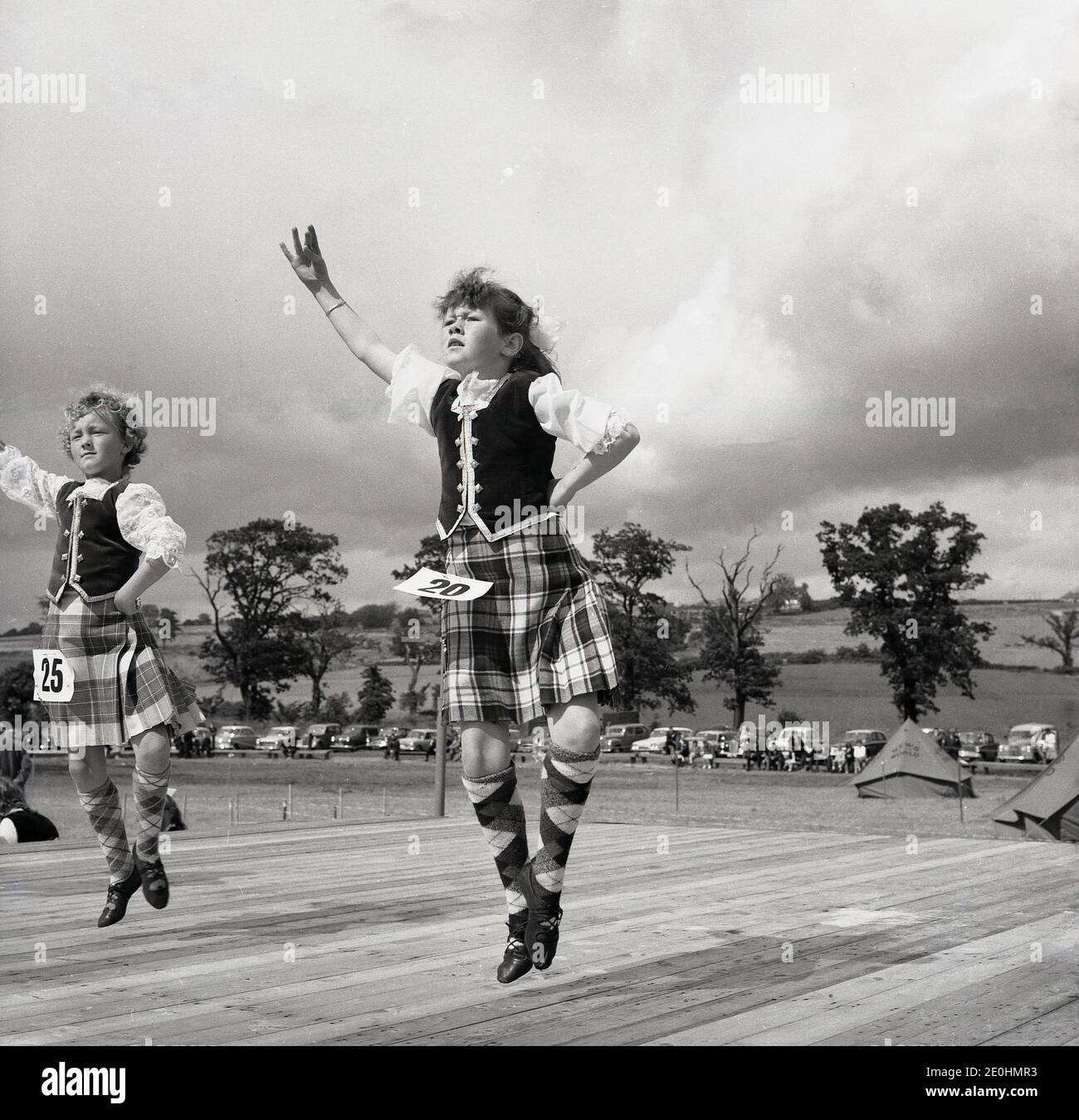 1960er Jahre, historisch, zwei junge Mädchen tanzen auf einer hölzernen Plattform oder Bühne draußen in einem Wettbewerb bei einem Highand Games, Schottland, Großbritannien. Obwohl das „Aboyne-Kleid“, die Westen, die Bluse und der Tartanrock für die schottischen Nationaltänze, für den frauenstarken Highland-Tanz getragen werden, wird ein Kilt-basiertes Outfit, wie hier zu sehen, getragen. Stockfoto