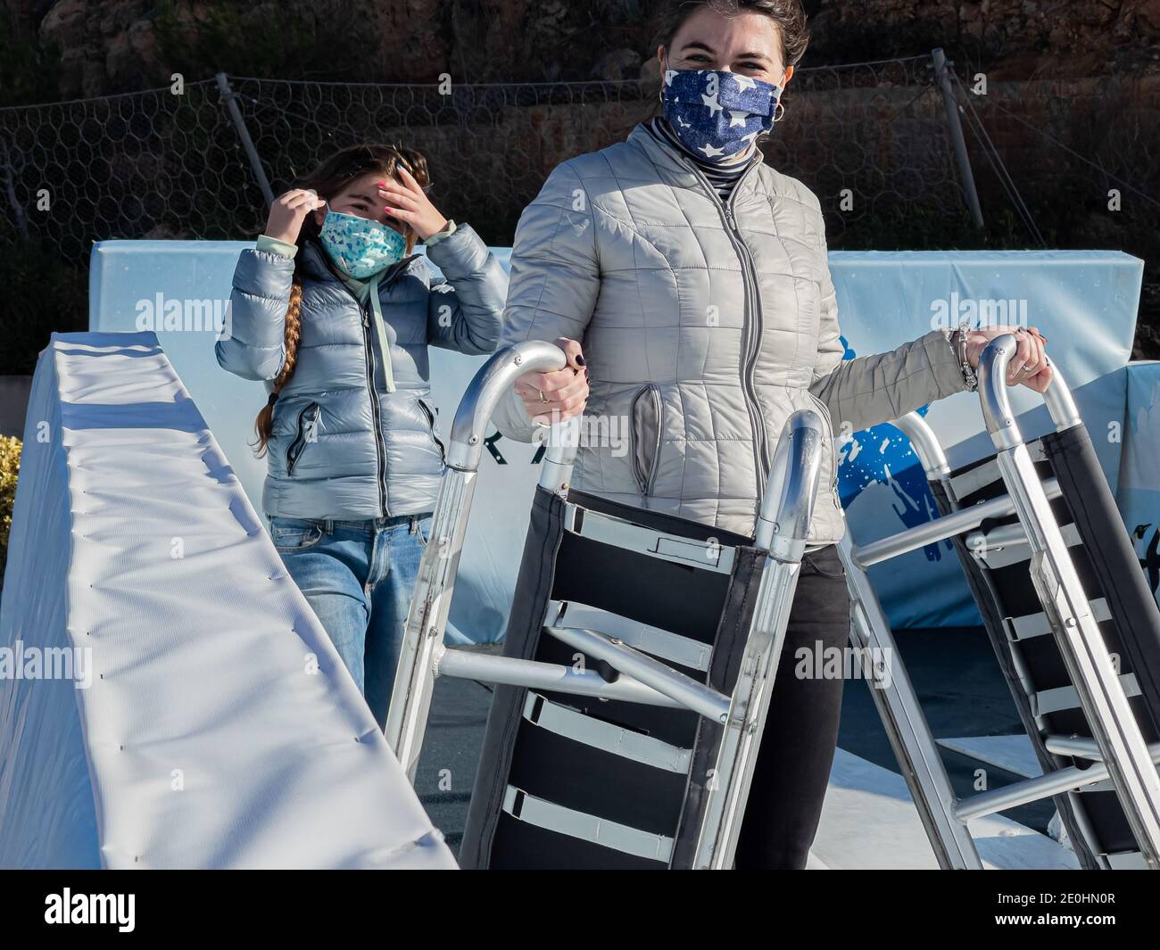 Mutter und Tochter tragen medizinische Maske während Schlitten auf Eis Rutsche während Covid-19 Pandemie in Port Adriano, Mallorca. Stockfoto