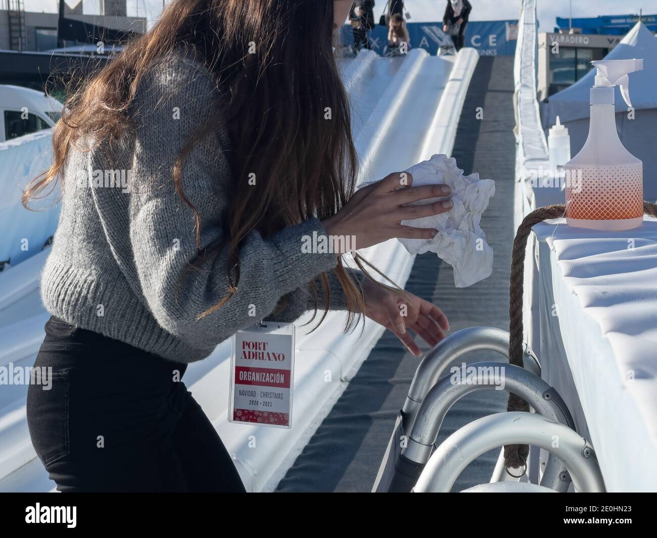 Junge Frau trägt medizinische Maske während der Desinfektion Schlitten auf Eis Rutsche während Covid-19 Pandemie in Port Adriano, Mallorca. Stockfoto
