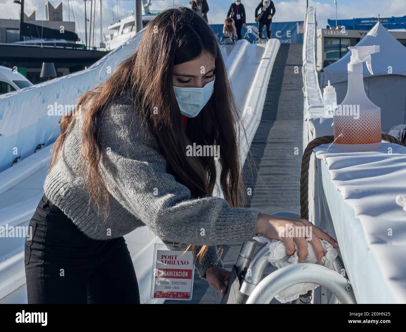 Junge Frau trägt medizinische Maske während der Desinfektion Schlitten auf Eis Rutsche während Covid-19 Pandemie in Port Adriano, Mallorca. Stockfoto