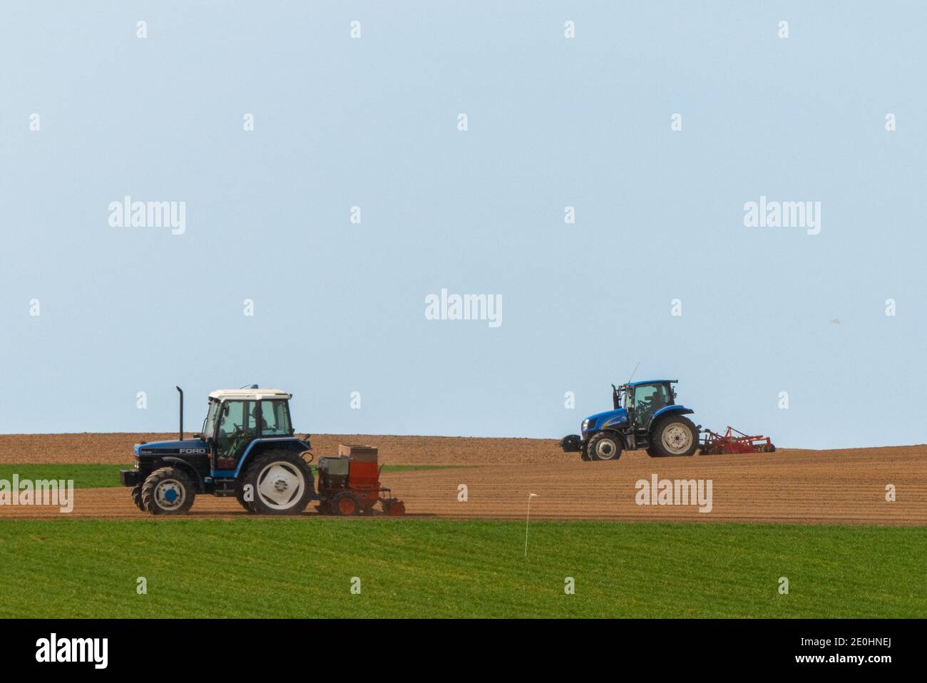 Zwei blaue Traktoren pflügen Felder und säen Getreide in der Auf dem Land Stockfoto