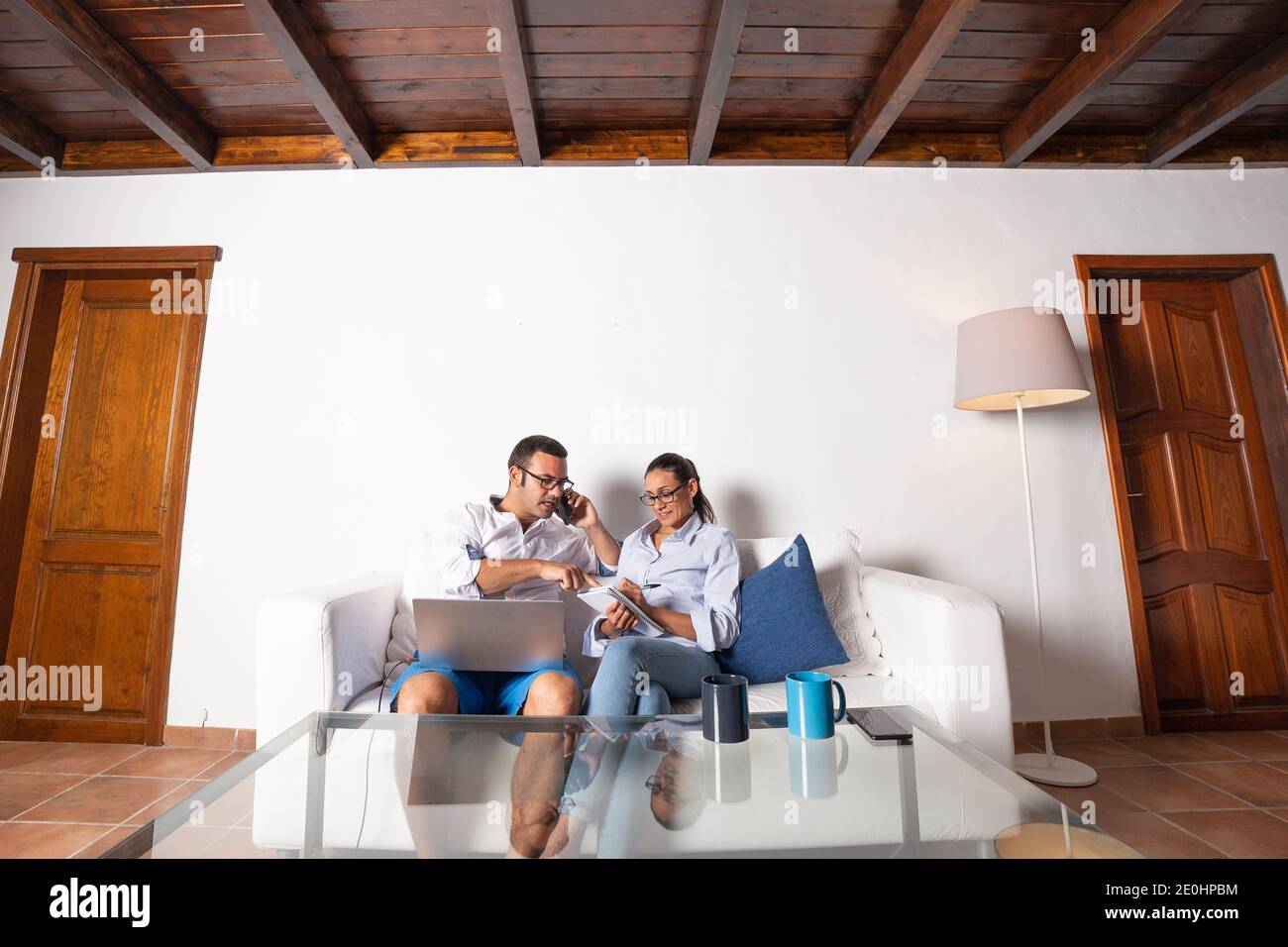 Junge Erwachsene Paar arbeitet online im Wohnzimmer zu Hause, Notizen mit dem Computer und Handy. Stockfoto