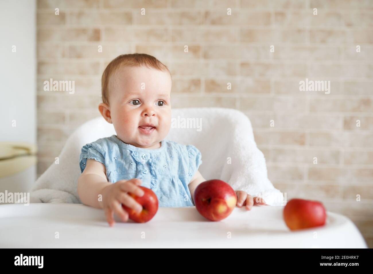 Smilling Baby essen Obst. Kleines Mädchen beißt gelben Apfel sitzen in weißen Hochstuhl in der sonnigen Küche. Gesunde Ernährung für Kinder. Feste Nahrung für mich Stockfoto