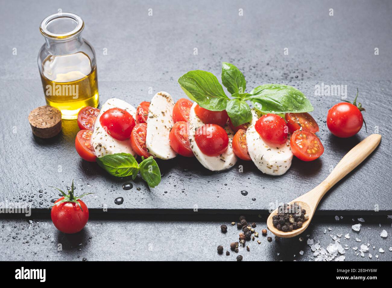 Mozzareela, Tomate und Basilikum, auf Tafel auf schwarzem Hintergrund, mit nativem Olivenöl extra, Salz und Pfeffer. Mediterrane Ernährung und gesunde Ernährung Stockfoto