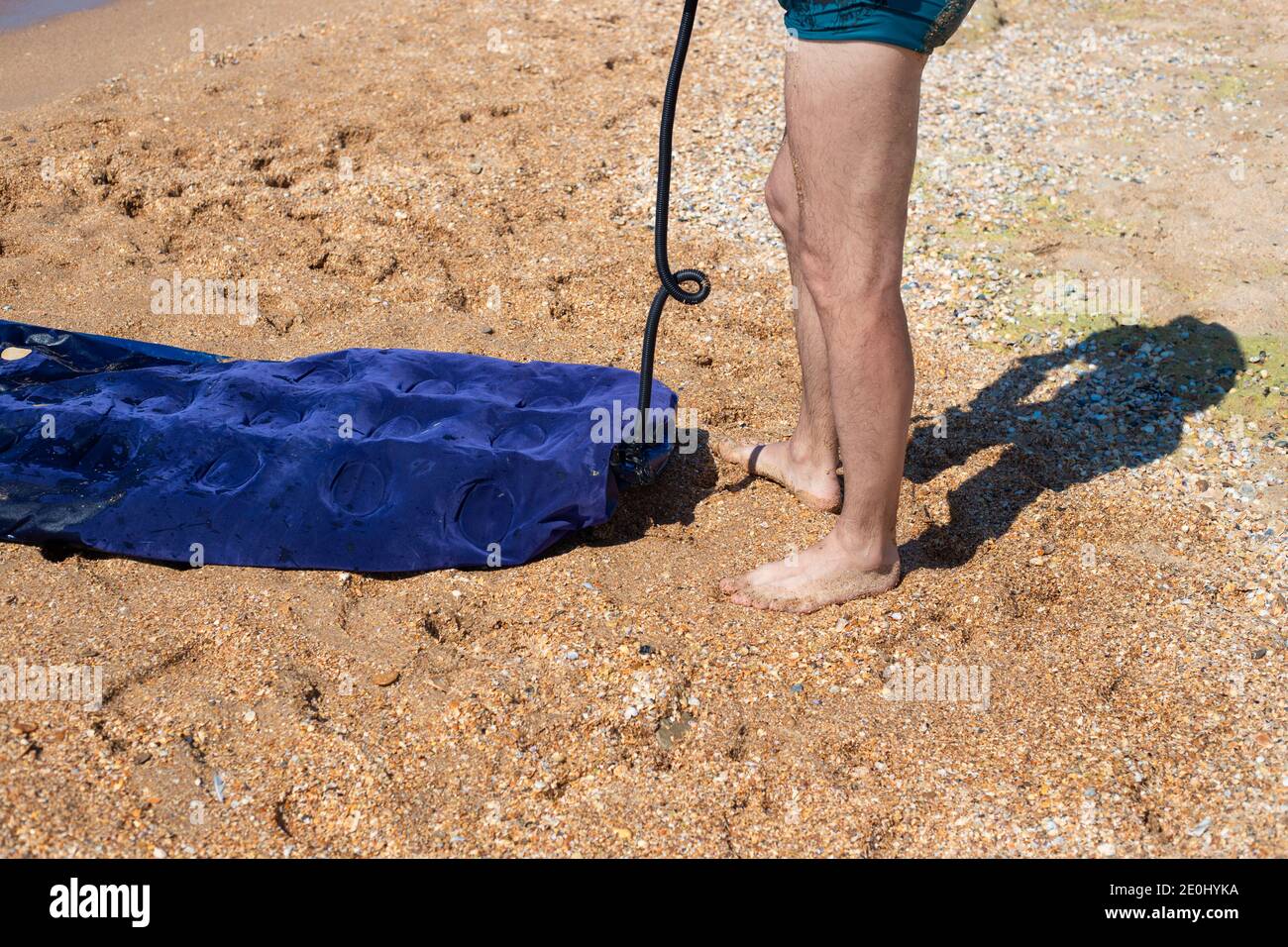 Ein Mann in Badehosen pumpt eine Gummimatratze auf den Sand, an der Küste. Schwimmen auf aufblasbaren Booten. Spaß im Sommer Stockfoto