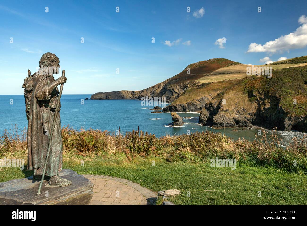 Die Statue des Heiligen Carannog wacht über die Bucht von Llangrannog, mit Bicas Zahn und der Landzunge von Ynys Lochtyn im Hintergrund. Stockfoto