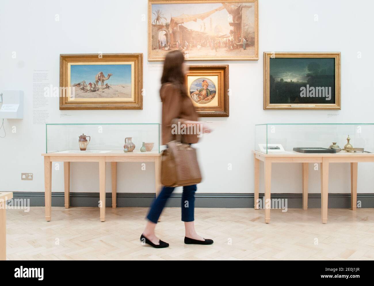 Allein weiße junge Frau, die in einer Kunstgalerie an Ölgemälden vorbeigeht, ist verschwommen und zeigt Bewegungen, während sie ihren Kopf dreht, um die Kunstwerke anzusehen Stockfoto
