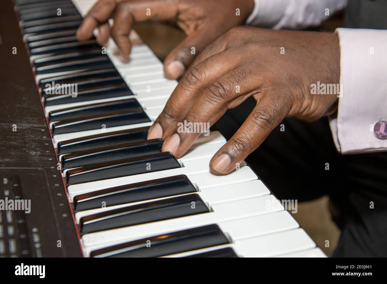 Finger eines alten afroamerikanischen Mannes, der eine Tastatur spielt Klavier in einem schwarzen Anzug und rosa Hemd Stockfoto