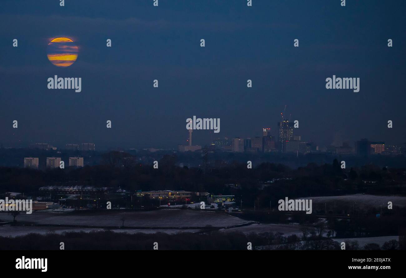 Birmingham, Großbritannien. 30. Dezember 2020. Der letzte Vollmond des Jahres 2020 bricht durch die Wolken, als er seinen Auftritt über einem schneebedeckten Stadtzentrum von Birmingham beginnt. Kredit: Lee Hudson Stockfoto