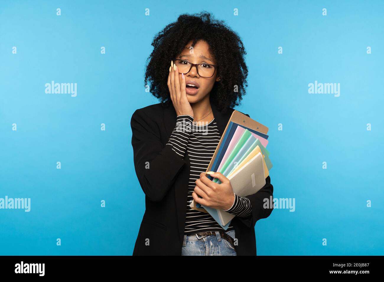 Afro-Studentin hält Ordner und Papier-Notizbücher, vergessen, eine Vorlesung zu lernen, nicht für Prüfungen vorbereitet, schlief durch Klassen am Institut, tut Stockfoto