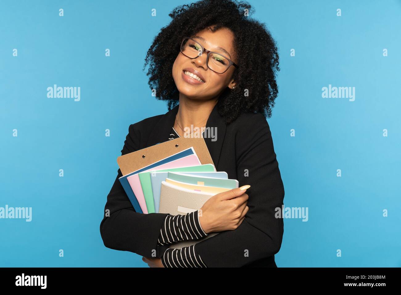 Fröhlicher Student in Blazer, tragen Sie eine Brille, halten Notebooks, Dokumente und Ordner, lächelnd Blick auf die Kamera isoliert auf blauen Studio Wand. Bildung in h Stockfoto