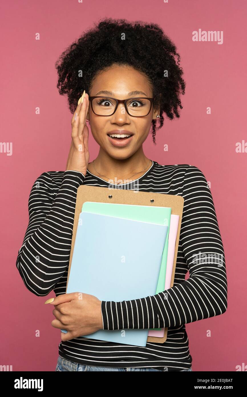 Junge glückliche afro-amerikanische Tutorin oder Lehrerin Frau isoliert auf rosa Studio Wand. Student Mädchen passt Brille hält Notebooks und lächelt. Bildung Stockfoto