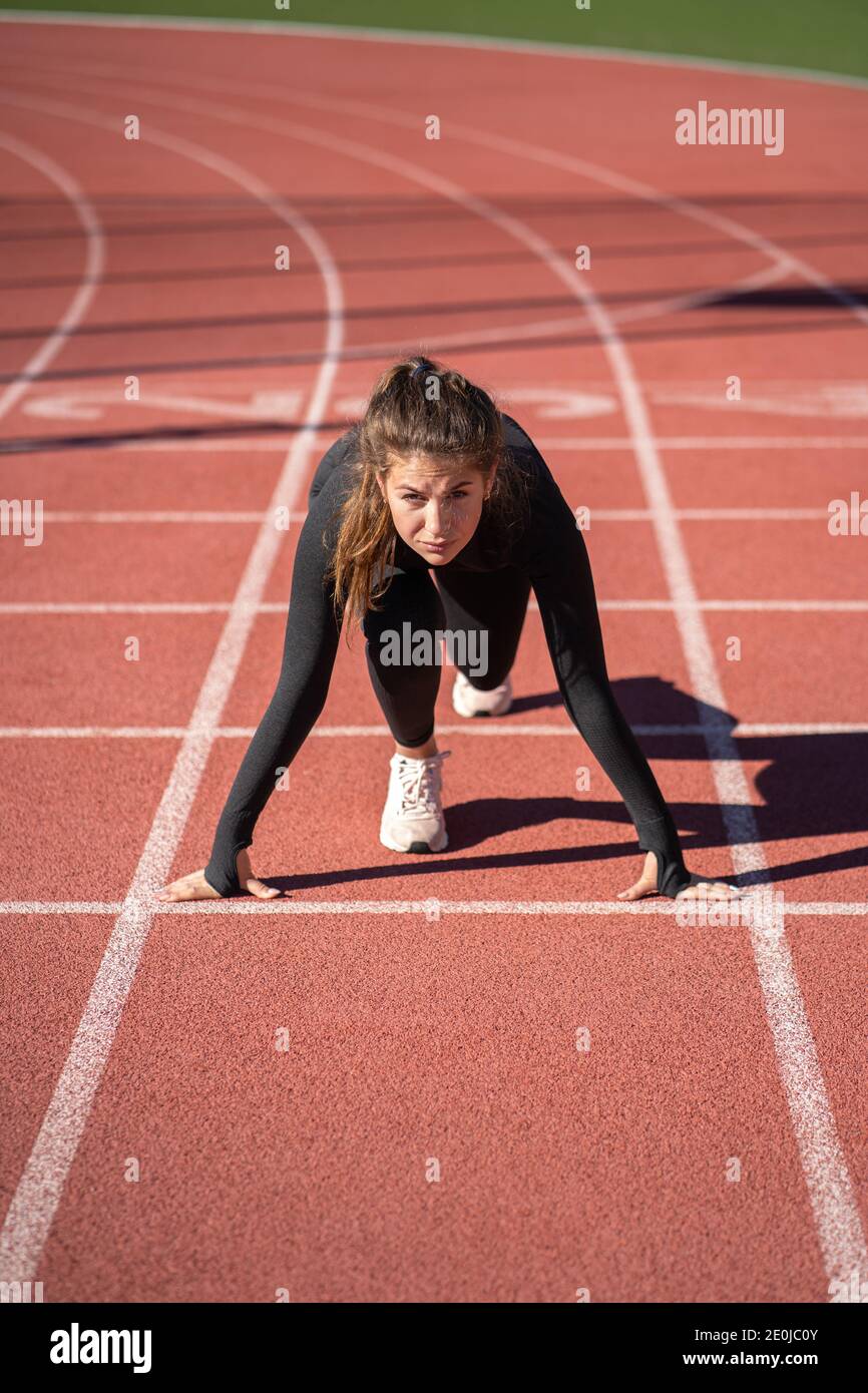 Selbstbewusste junge fit Frau Sprinter auf einem Laufband Gummistadion Oder Laufstrecke, die bereit ist, den Lauf zu starten Stockfoto