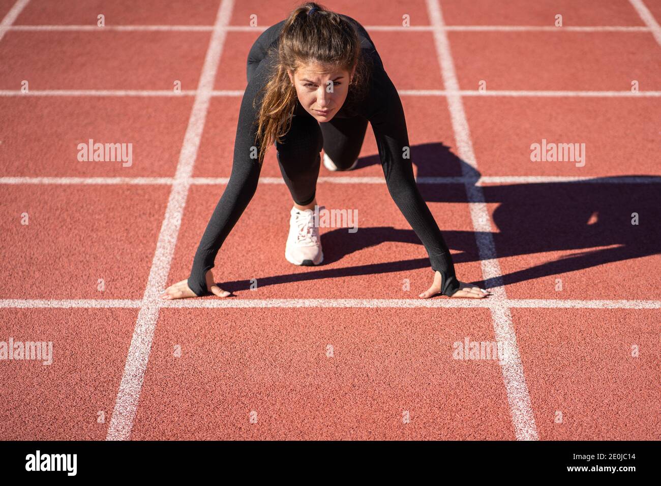 Selbstbewusste junge fit Frau Sprinter auf einem Laufband Gummistadion oder Laufstrecke immer bereit, laufen zu starten. Stockfoto