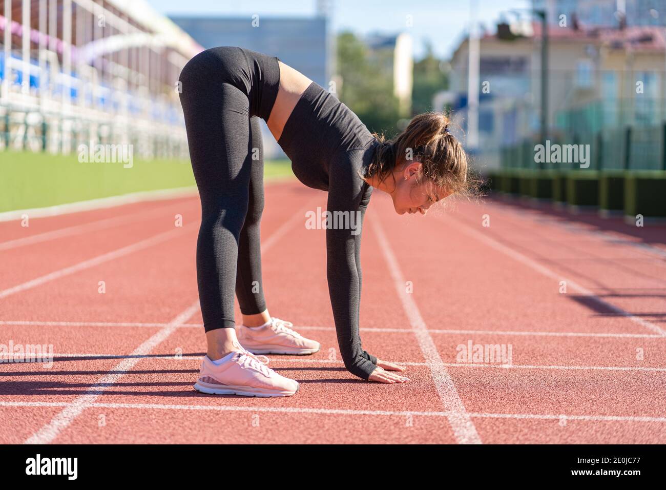 Fit junge Frau in schwarzer Sportbekleidung trainieren auf einem Laufband Gummi Stadion an sonnigen Sommertag, dabei stehen nach vorne falten Haltung, uttanasana pos Stockfoto