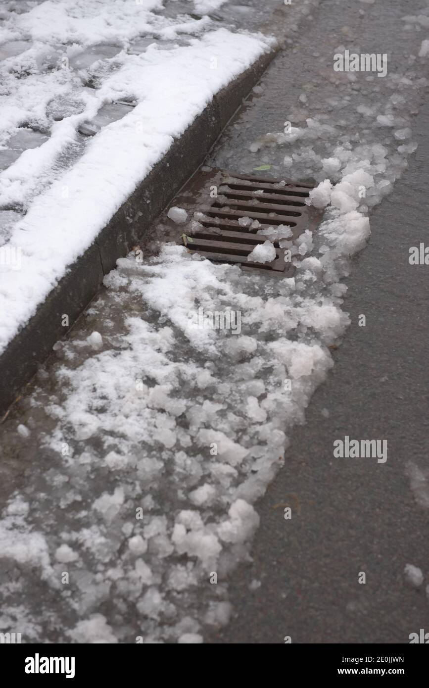 6 - Auftauen Schnee fließt in eine Metall-Bordwand Abfluss auf der  Oberfläche einer asphaltierten Straße. Track sichtbar, wo ein Auto durch  den Schnee gefahren hat Stockfotografie - Alamy