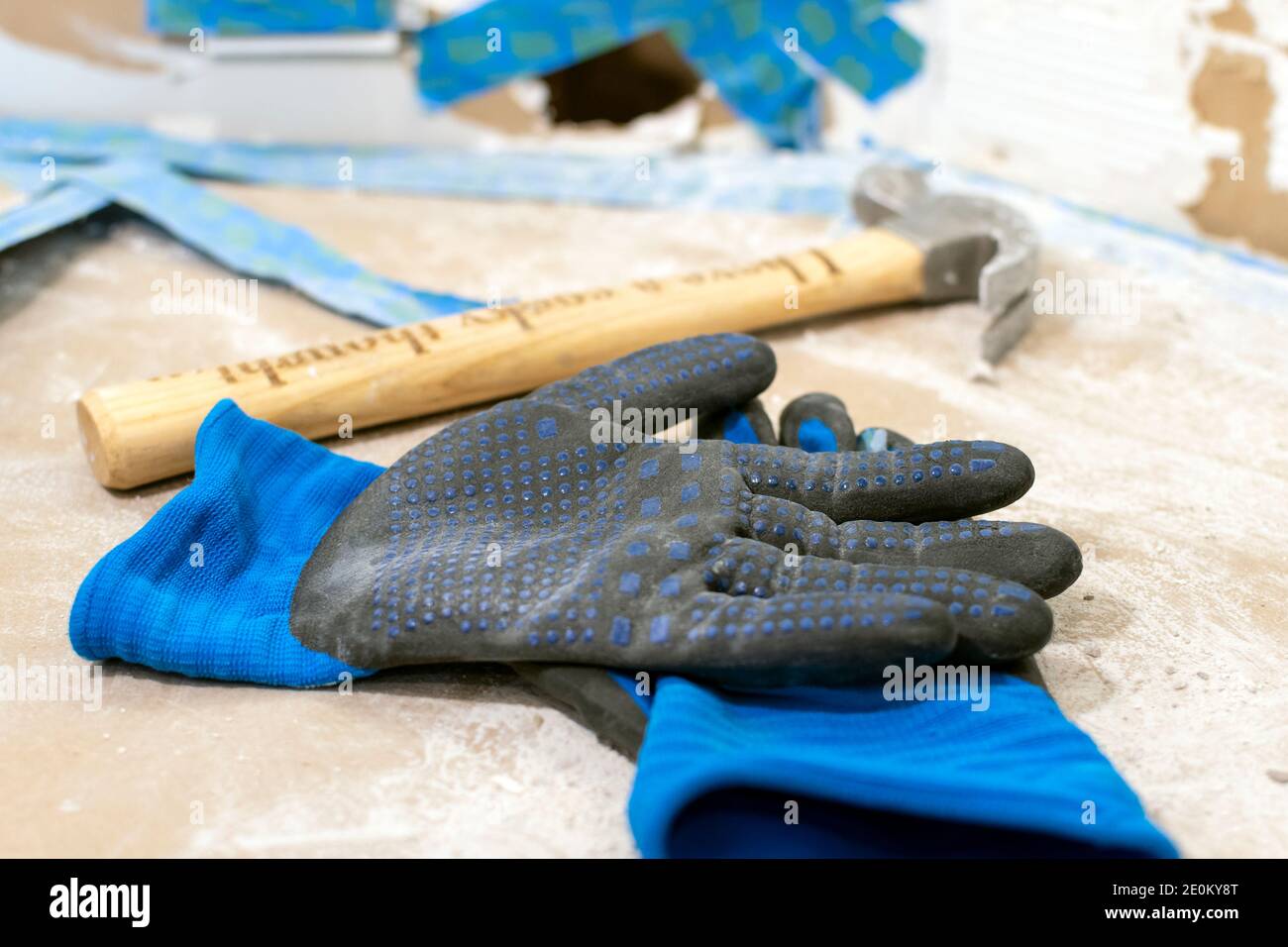Ein Paar schmutzige Handschuhe und ein Hammer liegen auf einer Theke mit einer Blechreparatur dahinter. Stockfoto