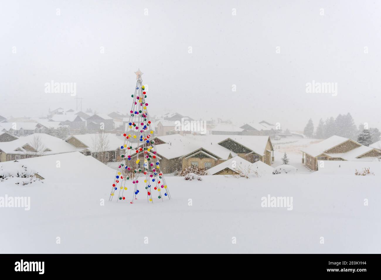 Ein schwerer Schneefall auf einem Hügel Haus mit einem beleuchteten dekorativen Weihnachtsbaum und eine Nachbarschaft von Häusern dahinter. Stockfoto