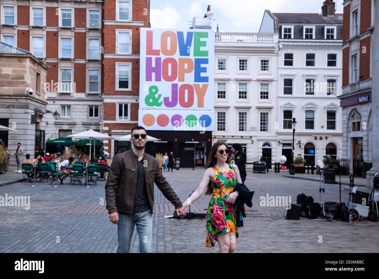 Ein glückliches Paar, das in Covent Garden im Vordergrund spazierengeht Und eine große Leinwand auf dem Hintergrund, die Liebe lesen Hoffnung und Freude Stockfoto