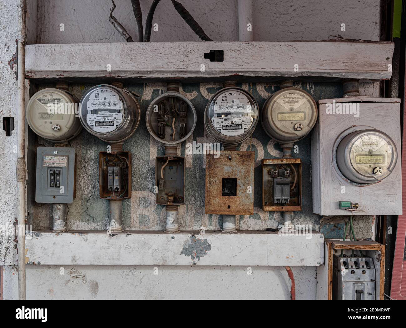Elektrische Messgeräte mit rostigen Geräten und freiliegenden Kabeln an einer Außenwand in Mexiko. Stockfoto