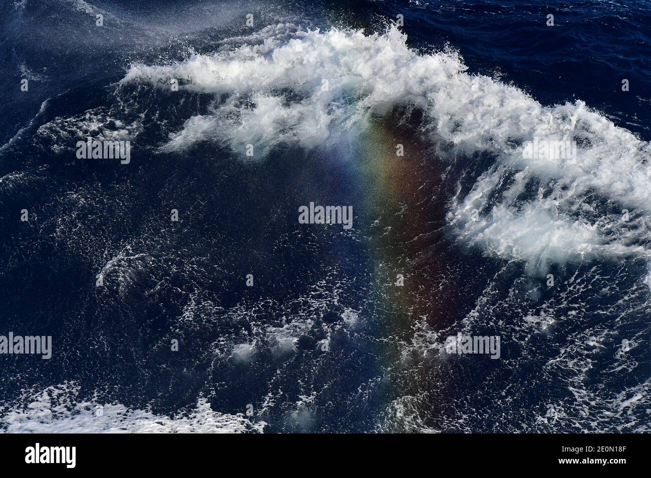 Wellen des Südatlantiks, die ihre immense Kraft und Stärke zeigen, koexistieren mit einem wunderschönen Regenbogen, der über den Kamm der Meereswellen reicht. Stockfoto