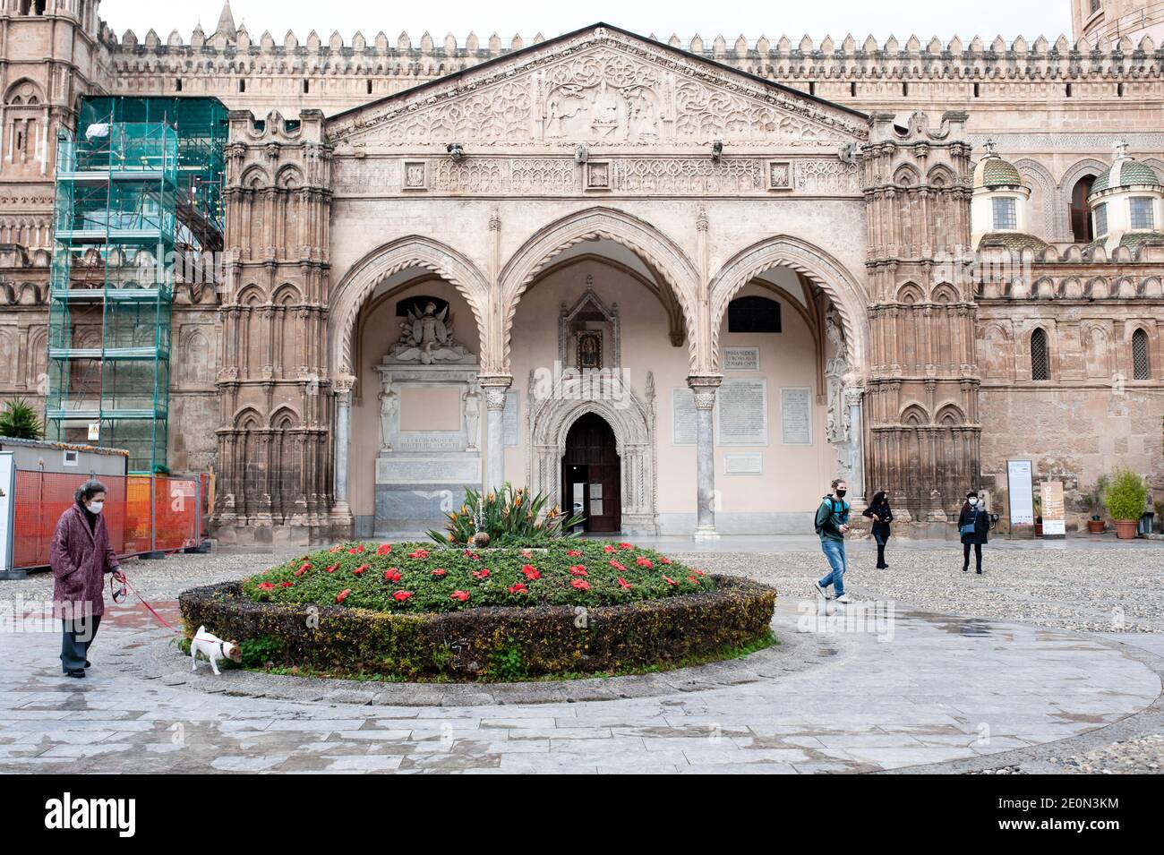 Eine Frau, die ihren Hund vor dem Silvesterabend in der Nähe des Eingangs der Kathedrale von Palermo führt. Viele gingen zu beliebten Orten und Märkten, wie das neue Jahr näherte. Stockfoto