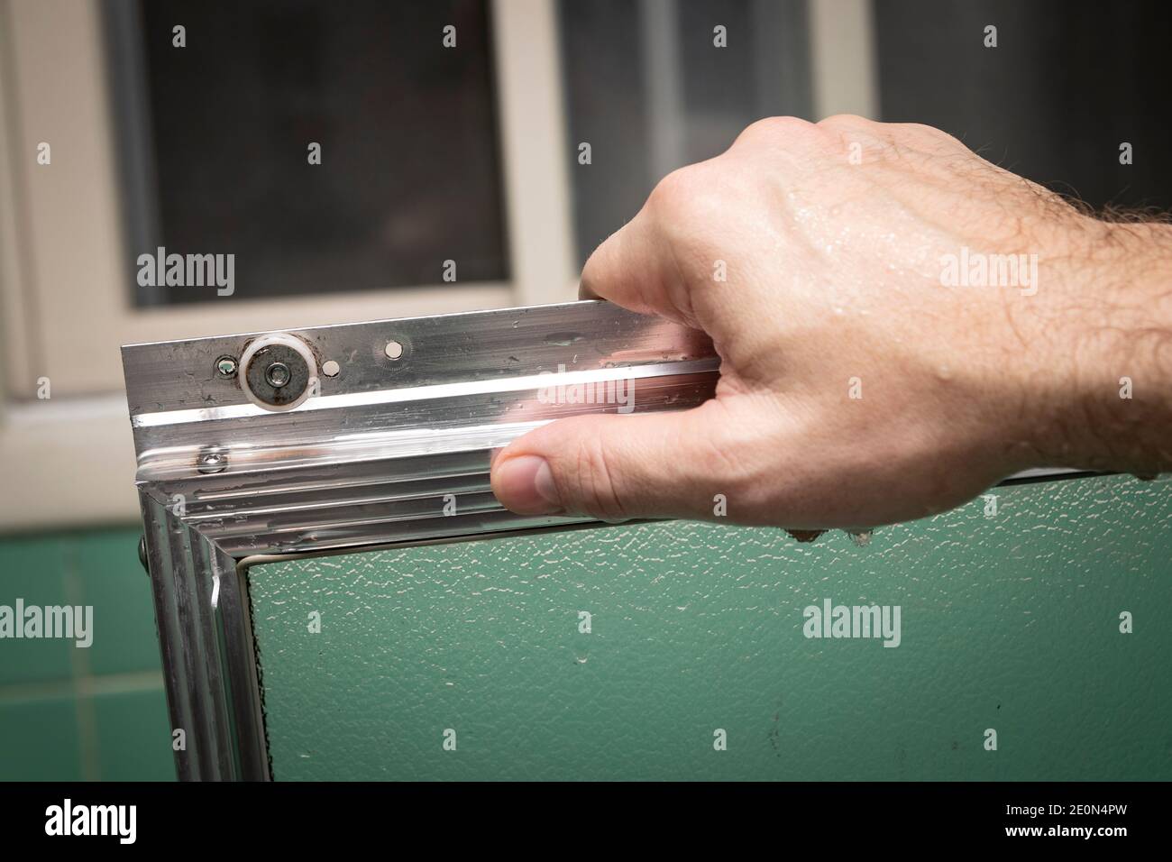 Hand hält sauber Schiebeduschtür Rahmen, in Retro-farbigen und gestylten Hause Bad Einstellung. Stockfoto