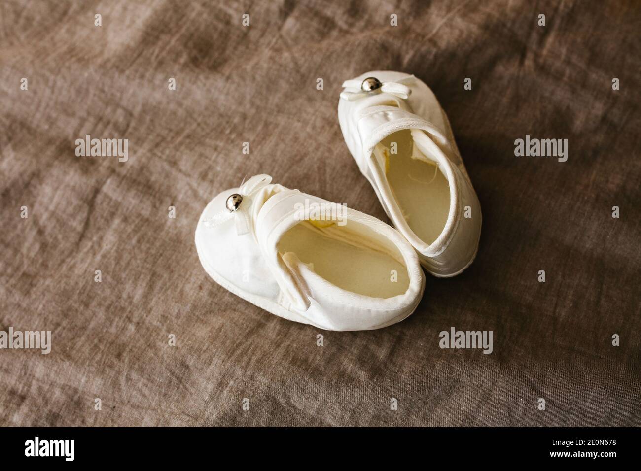 Weiße Babyschuhe auf braunem Hintergrund. Schuhe für ein Neugeborenes oder Baby. Stockfoto