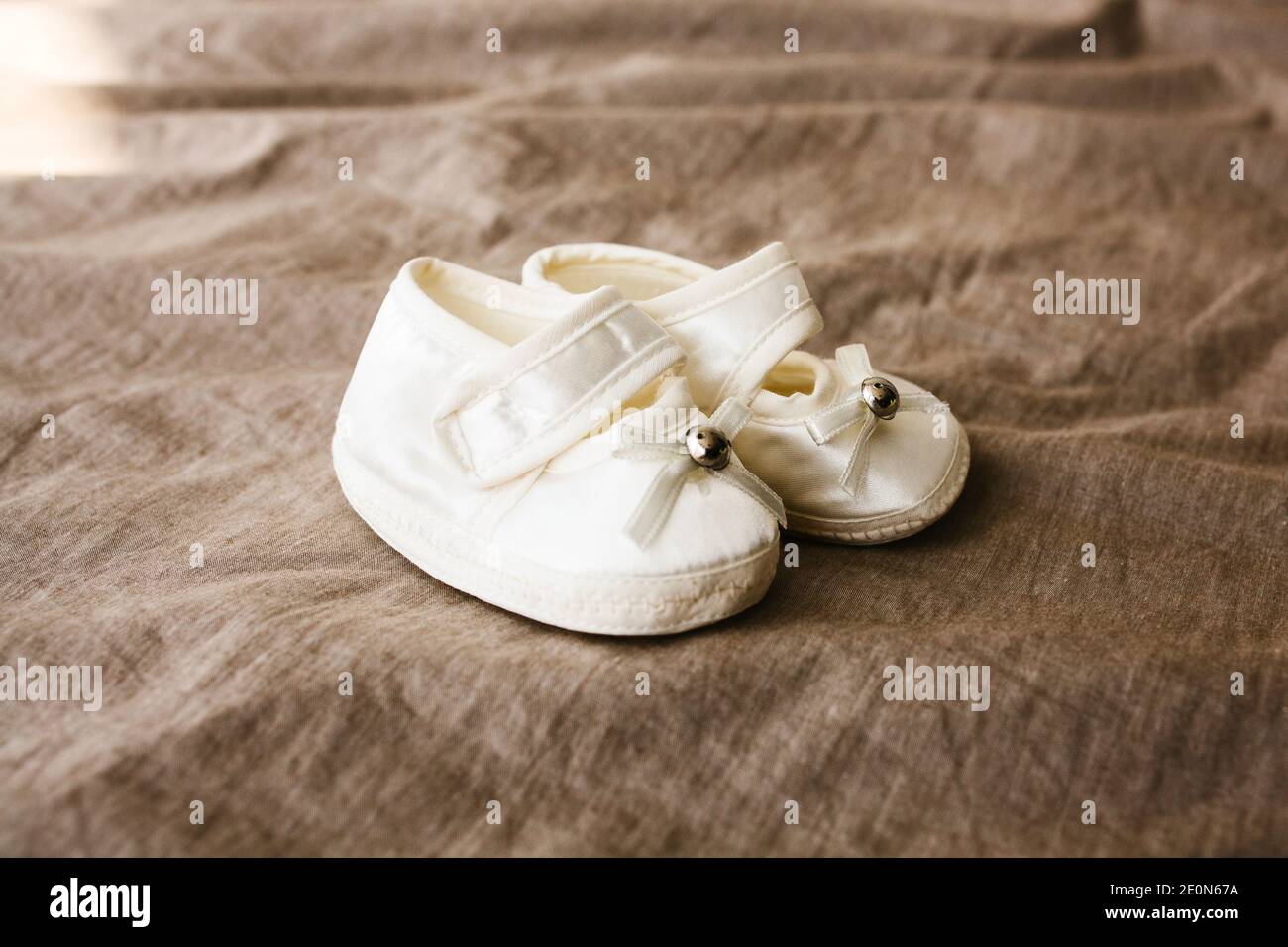 Weiße Babyschuhe auf braunem Hintergrund. Schuhe für ein Neugeborenes oder Baby. Stockfoto