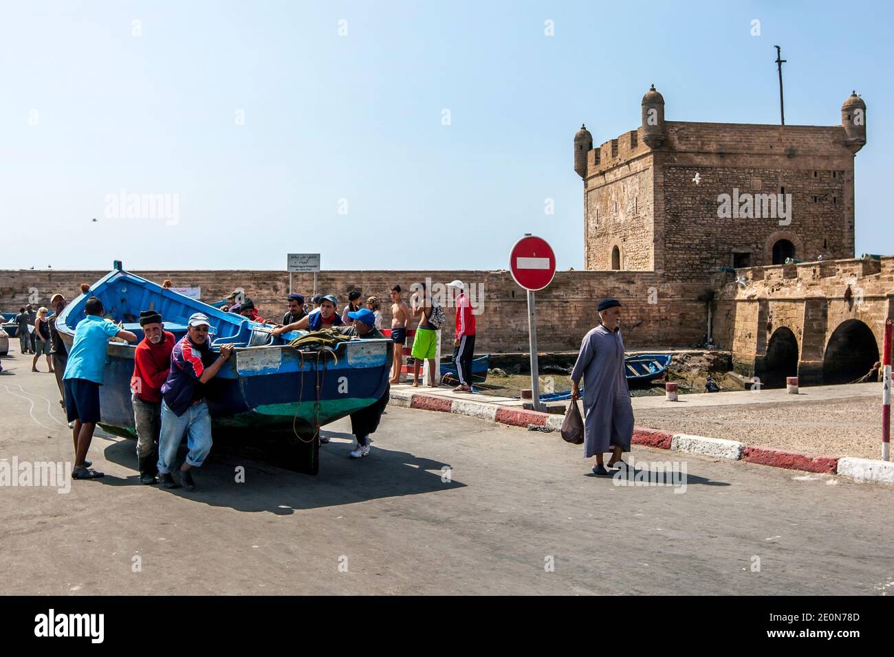 Die Fischer benutzen rohe Gewalt, um ein Boot entlang der Anlegestelle am Fischereihafen von Essaouira am Atlantik von Marokko zu bewegen. Stockfoto