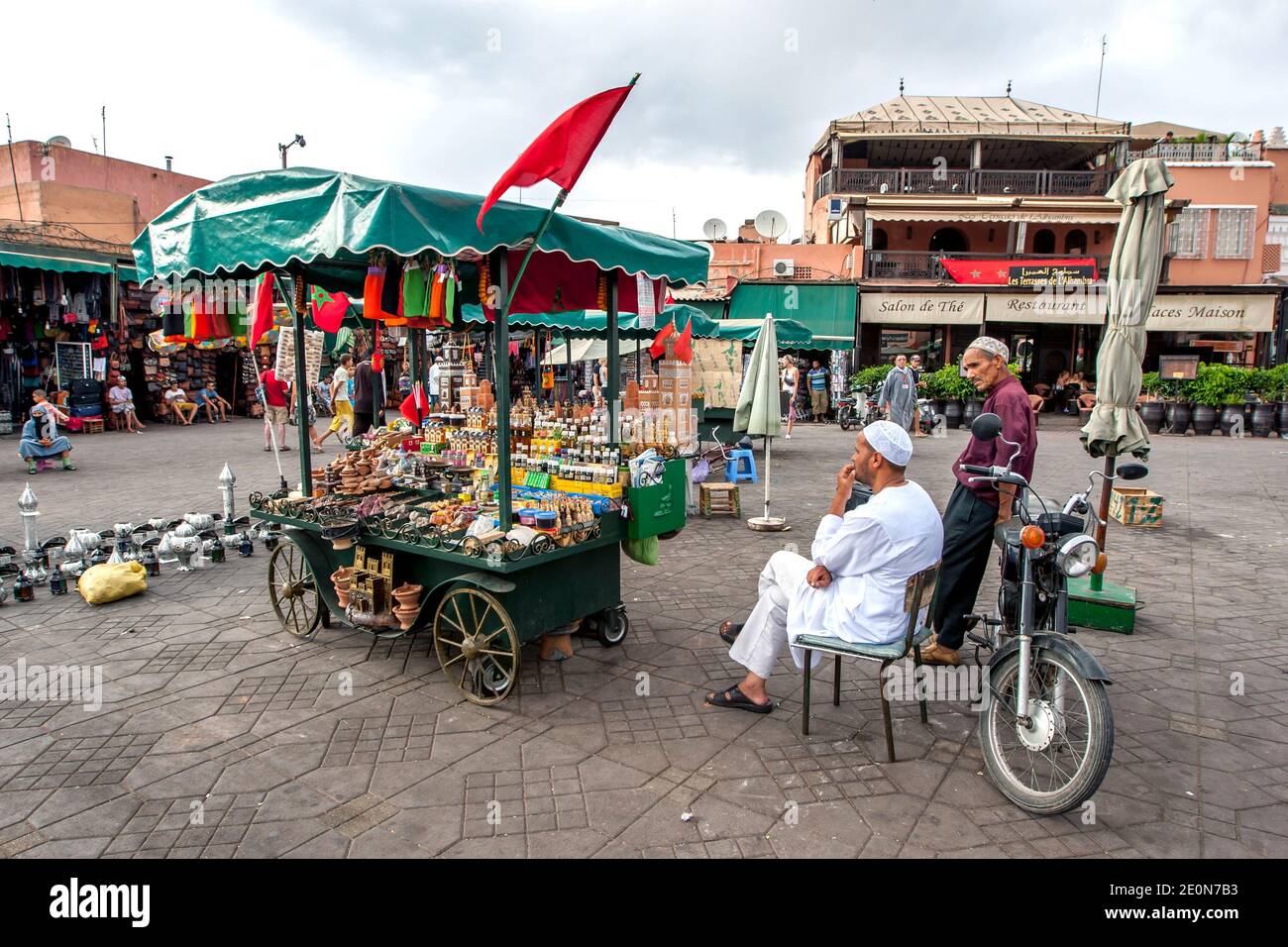 Ein Mann sitzt neben seinem tragbaren Stand und verkauft eine Vielzahl von Waren auf Djemaa el-Fna, dem Hauptplatz in der Medina von Marrakesch in Marokko. Stockfoto