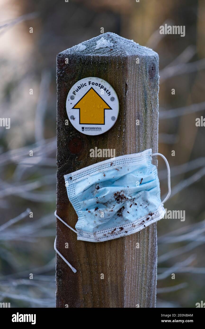 Eine weggeworfene Gesichtsmaske wird nach einem scharfen Frost über Nacht auf einem öffentlichen Fußweg in Großbritannien an einer Wegmarke des Fußweges festgeklebt. Stockfoto