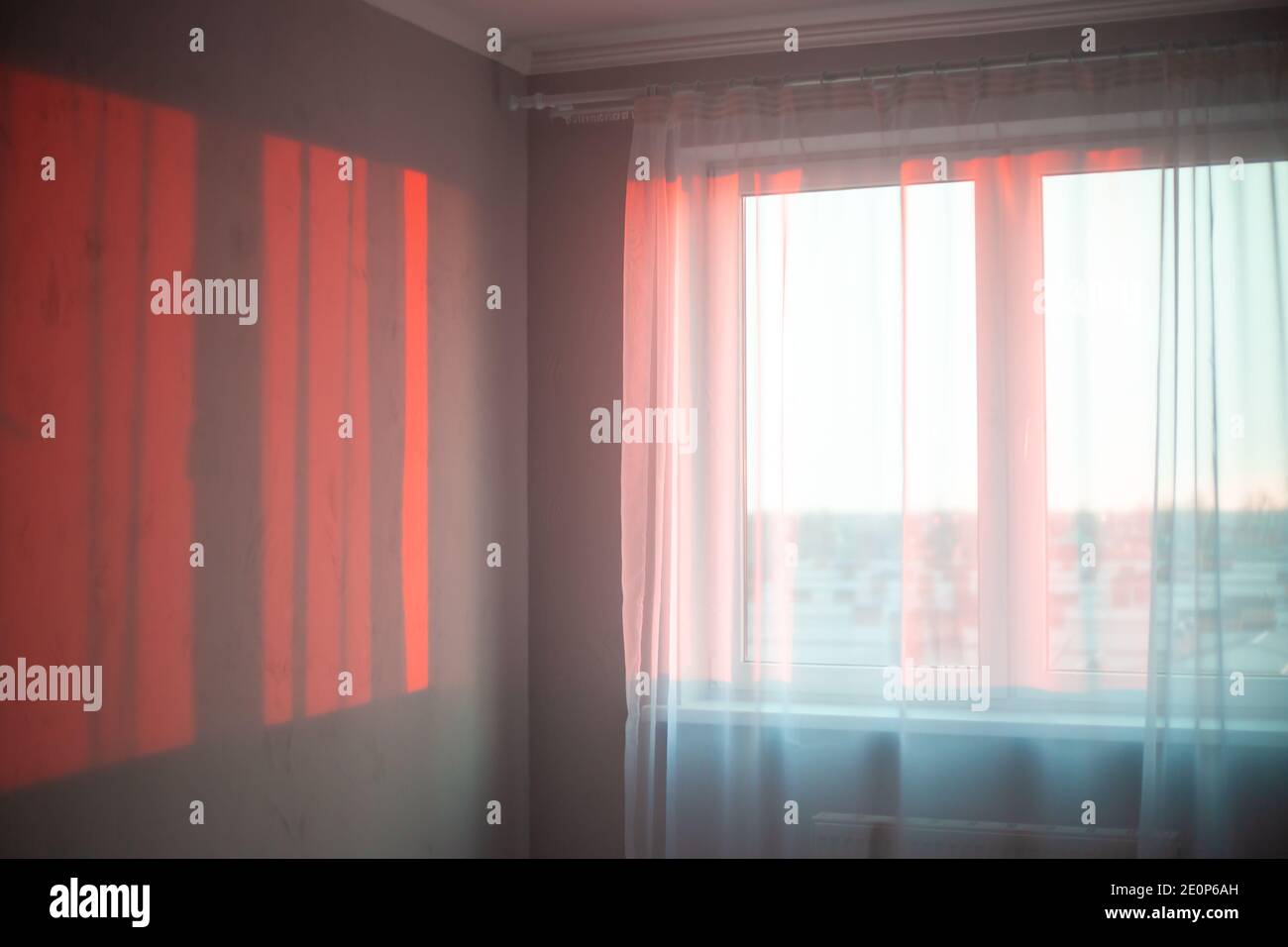 Die Strahlen der Morgensonne an der Wand in einem leeren Raum fallen durch den weißen Tüll auf dem Fenster. Neuer Tag, stimmungsvolle Stimmung. Stockfoto