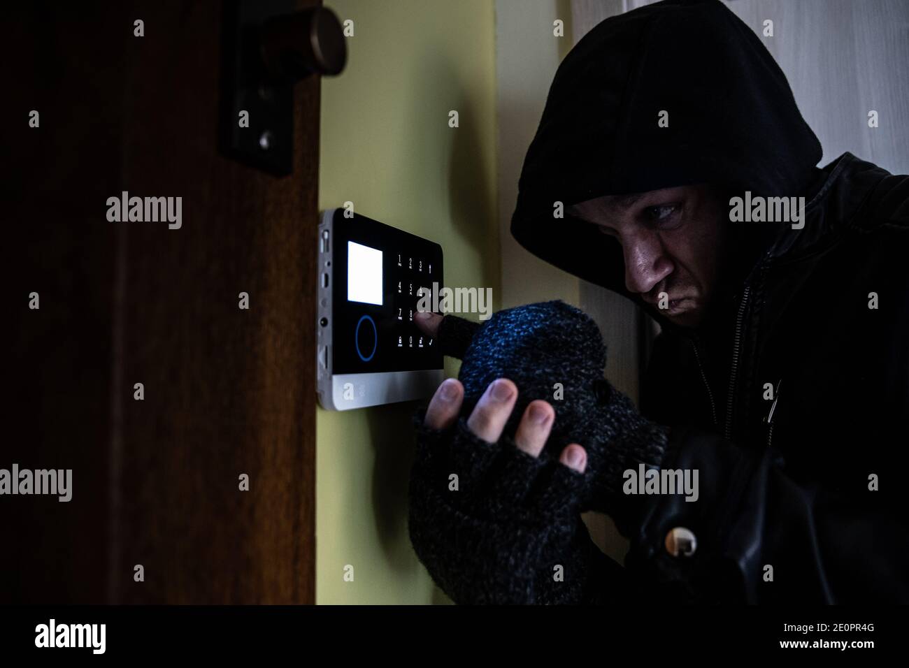 Ein Einbrecher mit Handschuhen und einer Kapuze auf dem Kopf versucht, die Alarmanlage zu entwaffnen. Stockfoto