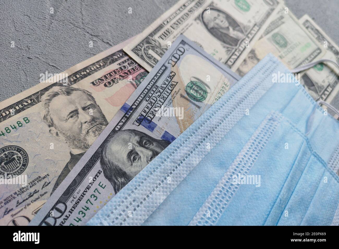 Amerikanische Dollar und blaue chirurgische Schutzmasken sind auf grauem Hintergrund. Geld befindet sich in einer modernen finanziellen Situation. Stockfoto