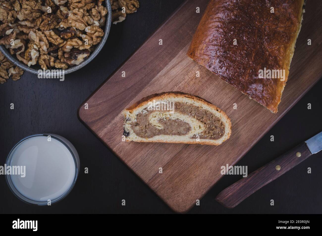 Hausgemachte Walnussrolle auf dem Holzschneidebrett. Frisch gebackene Walnussrolle mit einem Glas Milch bereit zum Frühstück. Traditionelle ungarische Torte. Stockfoto