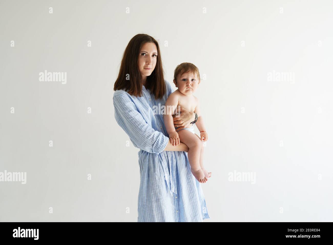 Portrait der schönen Dame in romantischen blauen Kleid und sie Süßes kleines Baby, das sich in eine vor der Kamera stehende Kamera freut Weiße Wand Stockfoto