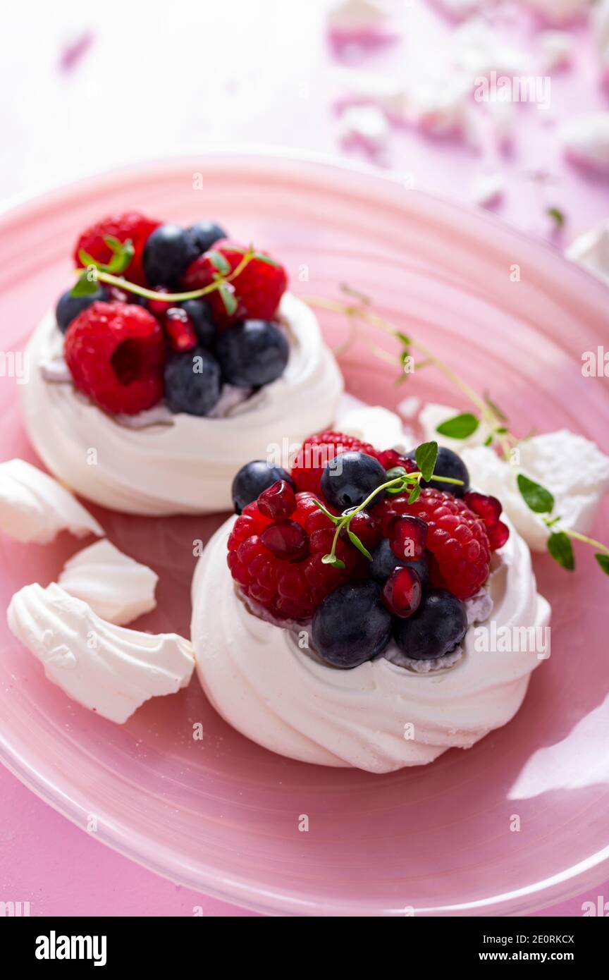 Pavlova-Baiser-Kuchen mit Beeren auf gestaubtem Zucker rosa Hintergrund Stockfoto