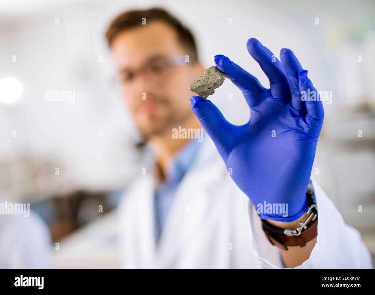Junge Wissenschaftler halten ein mineralisches Exemplar in einem blauen Schutzhandschuh Im Labor für Materialwissenschaft Stockfoto