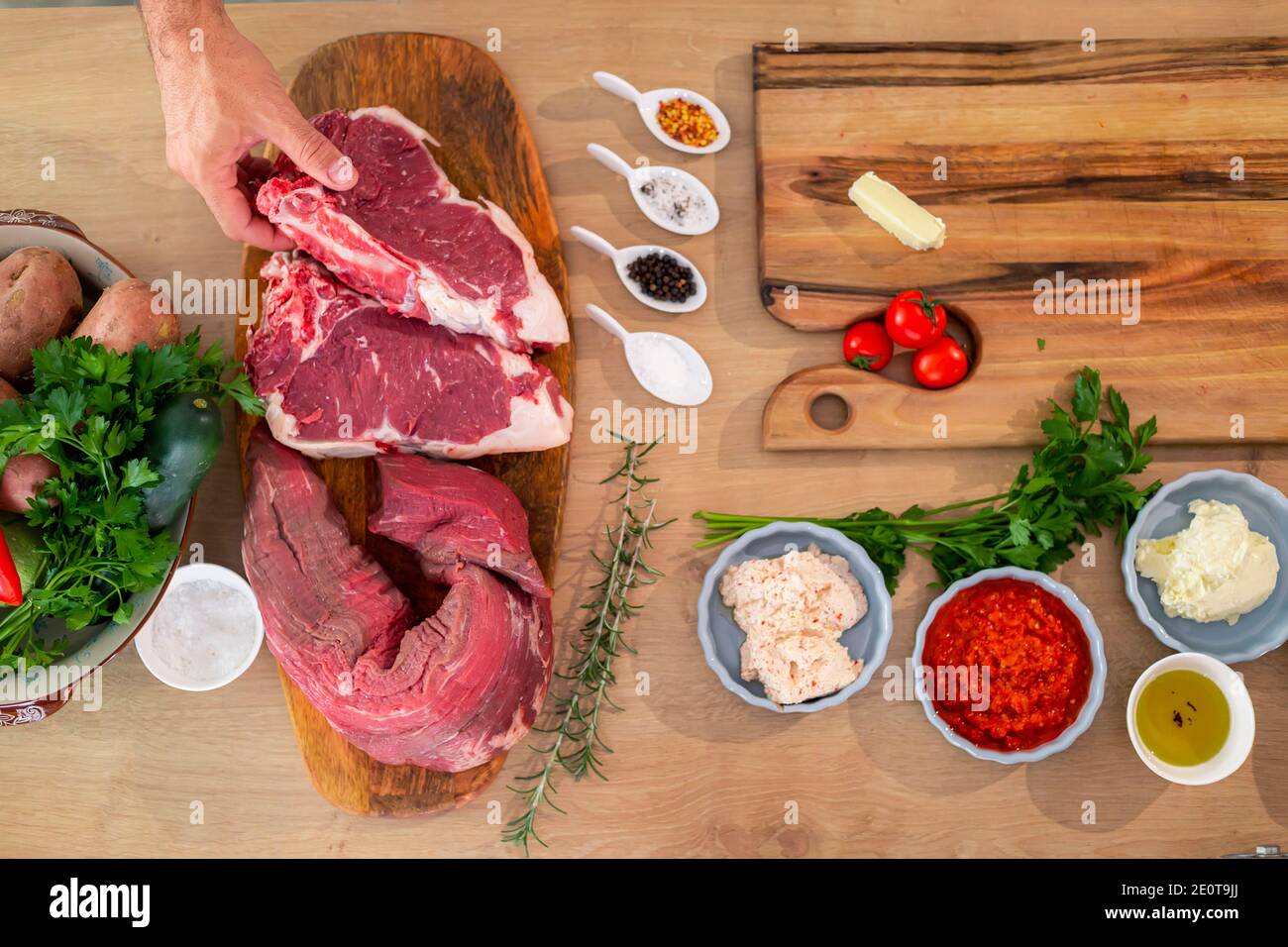 Fleischstücke, Gewürze und Gemüse von oben auf einem hölzernen Küchentafel fotografiert. Auf der Seite stehen Kartoffeln, Paprika und Kürbisse in einem Topf Stockfoto