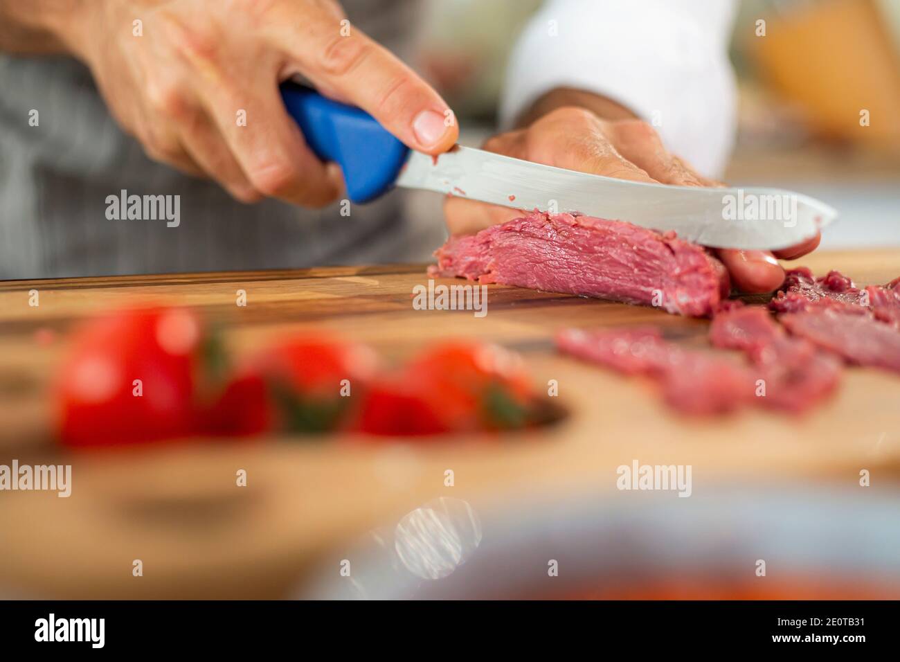 Eine Nahaufnahme der Hände des Küchenchefs, die während der Vorbereitungsphase Carpaccio-Fleisch auf einem Holzbrett in dünne Stücke schneiden. Verschiedene kleine Küche b Stockfoto