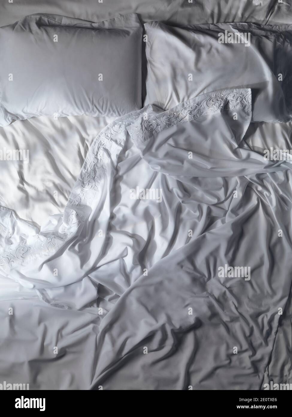 Ungemachtes leeres Bett, weiße Spitzen, unordentliche, zerknittert gefurtete Bettlaken und Kissen. Künstlerischer Hintergrund, Blick von oben. Stockfoto