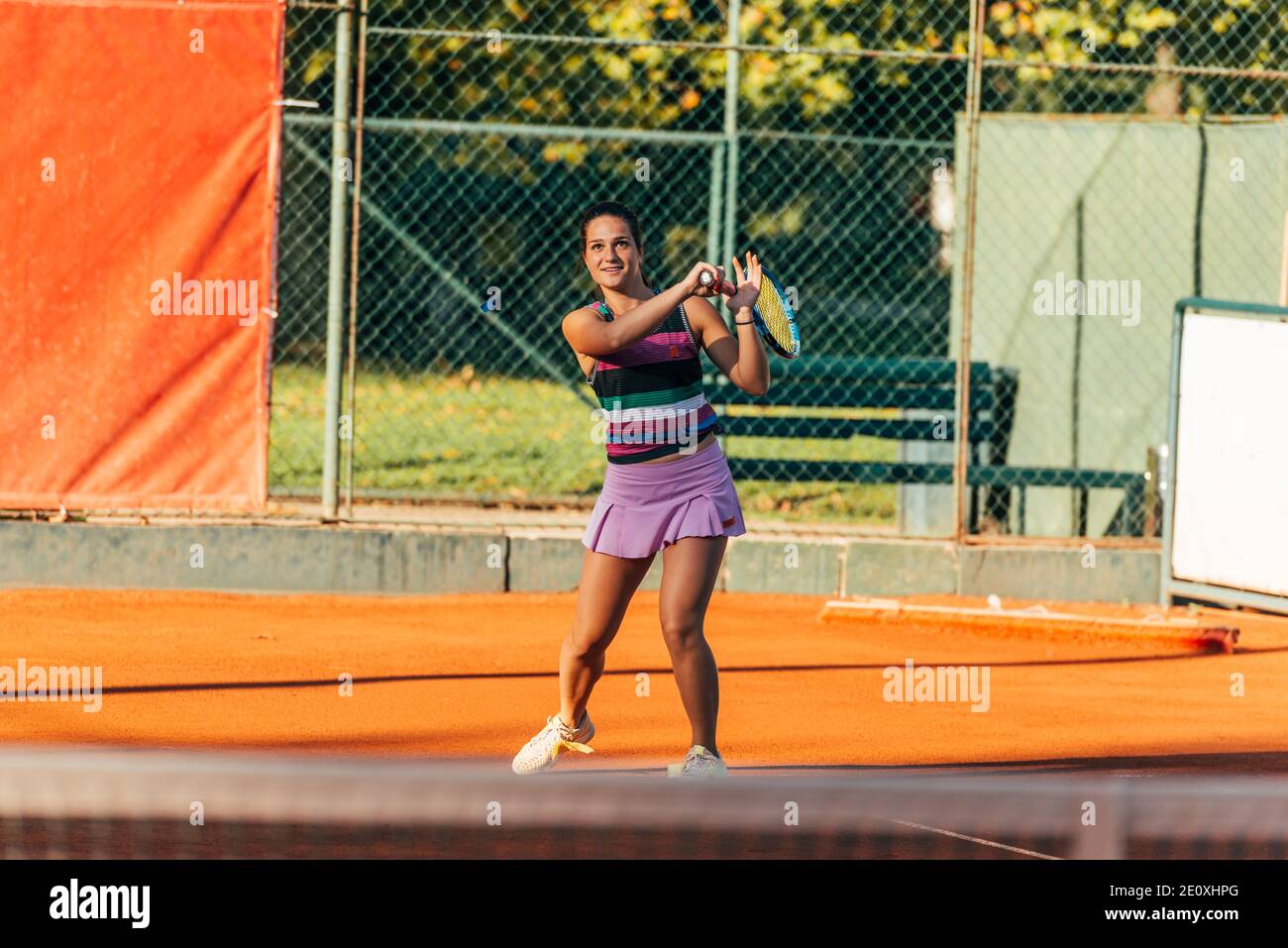 Eine junge, fit Frau spielt Tennis im Freien auf einer Orange Tennisplatz früh am Morgen Stockfoto