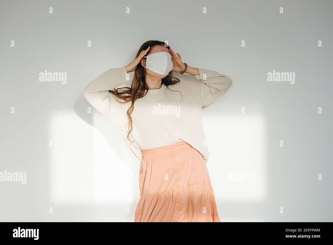 Denierin Frau in einem weißen sonnendurchfluteten Raum mit einer weißen Stoffmaske auf ihrem Gesicht. Stockfoto