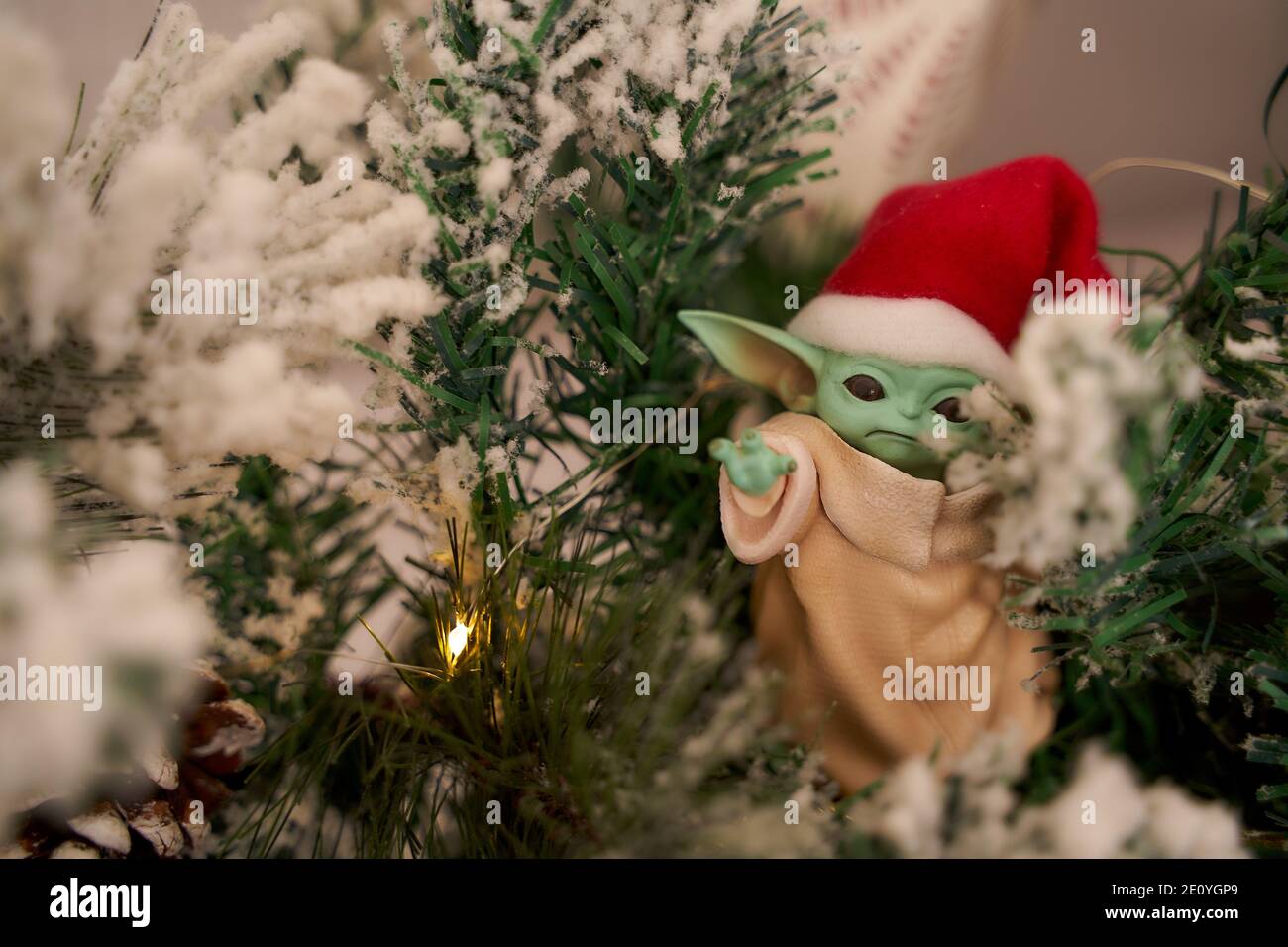 Dez, 2020: Darstellung von Baby Yoda, einer Action-Figur, die in einer roten Mütze auf weihnachtlichem Hintergrund steht. Bokeh-Effekt. Stockfoto