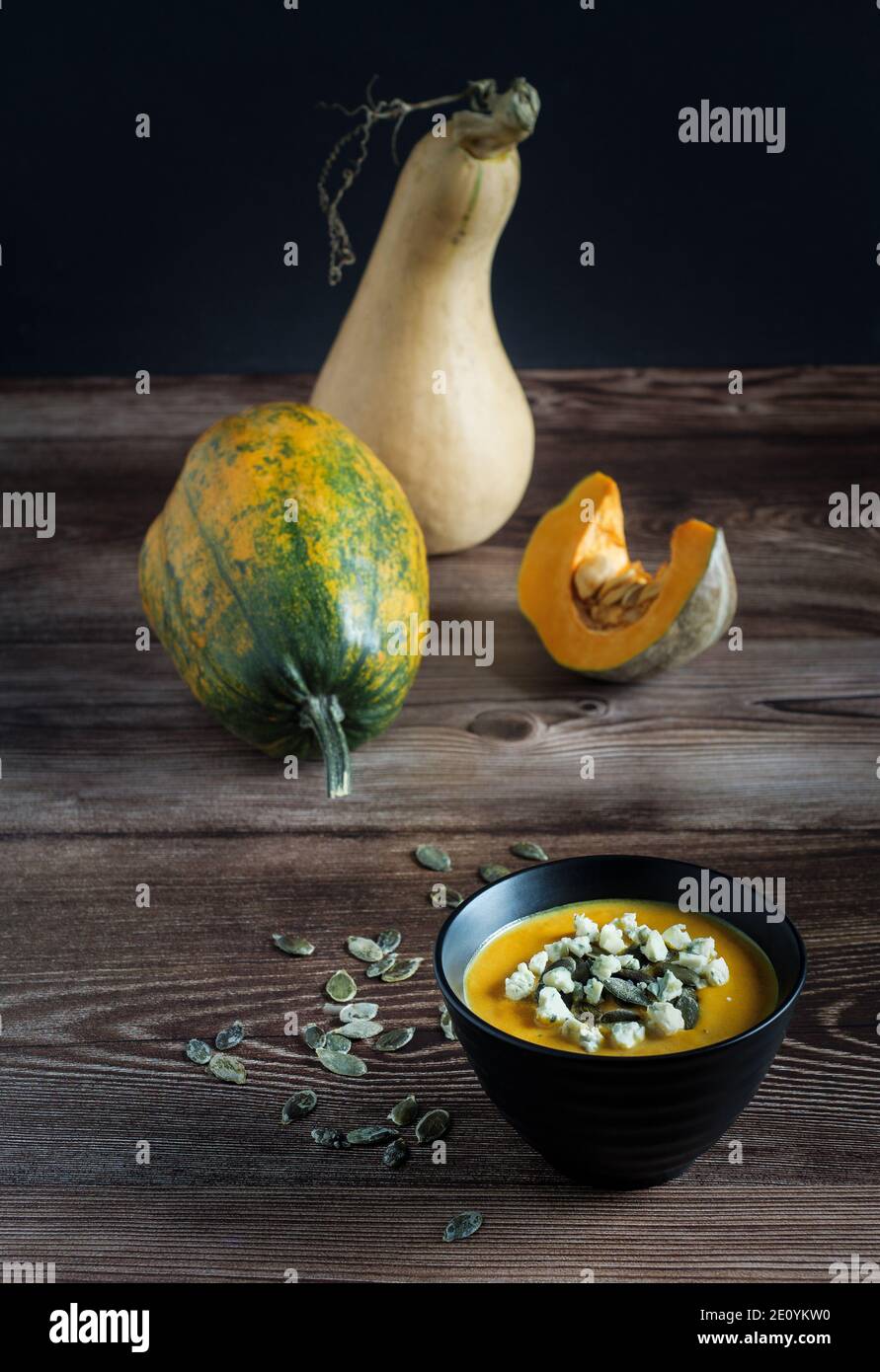 Kürbiscremesuppe mit blauem Käse und rohen Kürbissen auf Holztisch, Draufsicht. Stockfoto